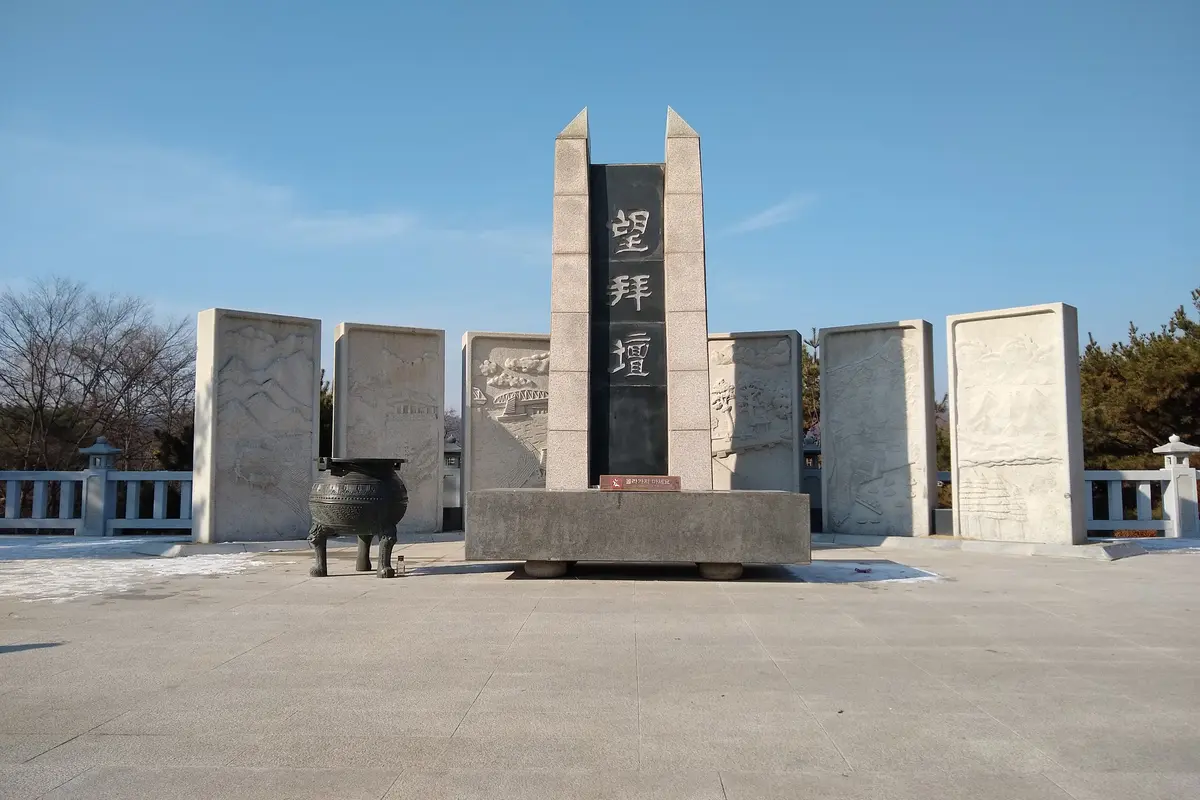 The Mangbaedan altar at Imjingak, a row of grey stone panels carved with reliefs around a tall black stone engraved with three Chinese characters, under a blue sky